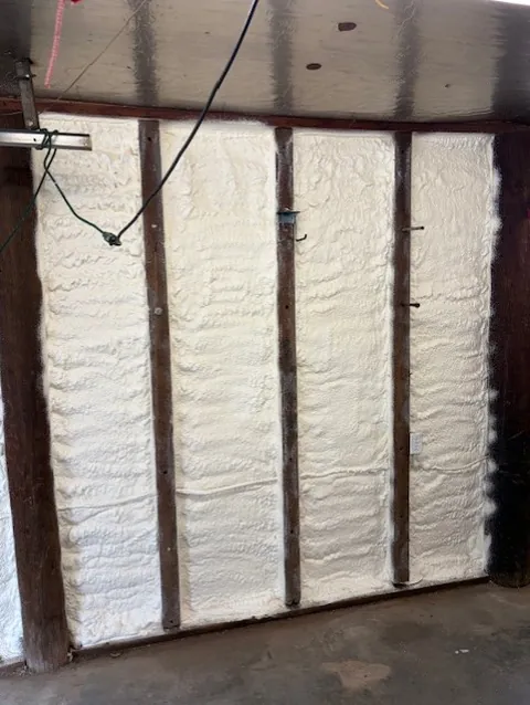 Close-up of closed-cell spray foam filling wall stud cavities evenly, ready to be trimmed flush